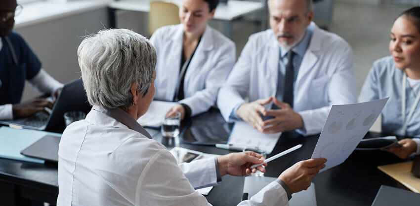 Female doctor holding up payor contract negotiation value proposition to colleagues