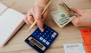 One hand holding money and another hand using calculator